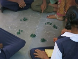 Students explore math manipulatives in small groups. They write directly on the floor using chalk.